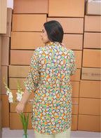 Woman in a patterned shirt standing in front of stacked cardboard boxes.