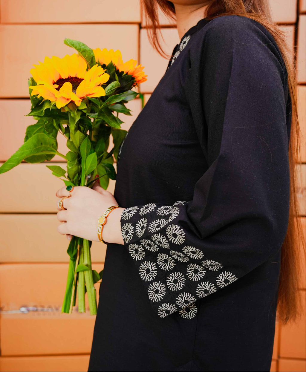 Person holding a bouquet of sunflowers wearing a dark blue outfit with floral embroidery.