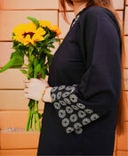Person holding a bouquet of sunflowers wearing a dark blue outfit with floral embroidery.