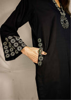 Black outfit with white floral embroidery on sleeves and back, held by a person.