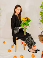 Woman in black outfit holding sunflowers with scattered oranges on a light background