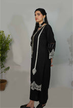 Woman wearing a black outfit with white embroidery against a plain background