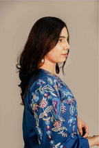 Woman wearing a blue embroidered dress against a beige background