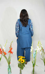 Woman in a blue outfit standing among flowers with a plain background