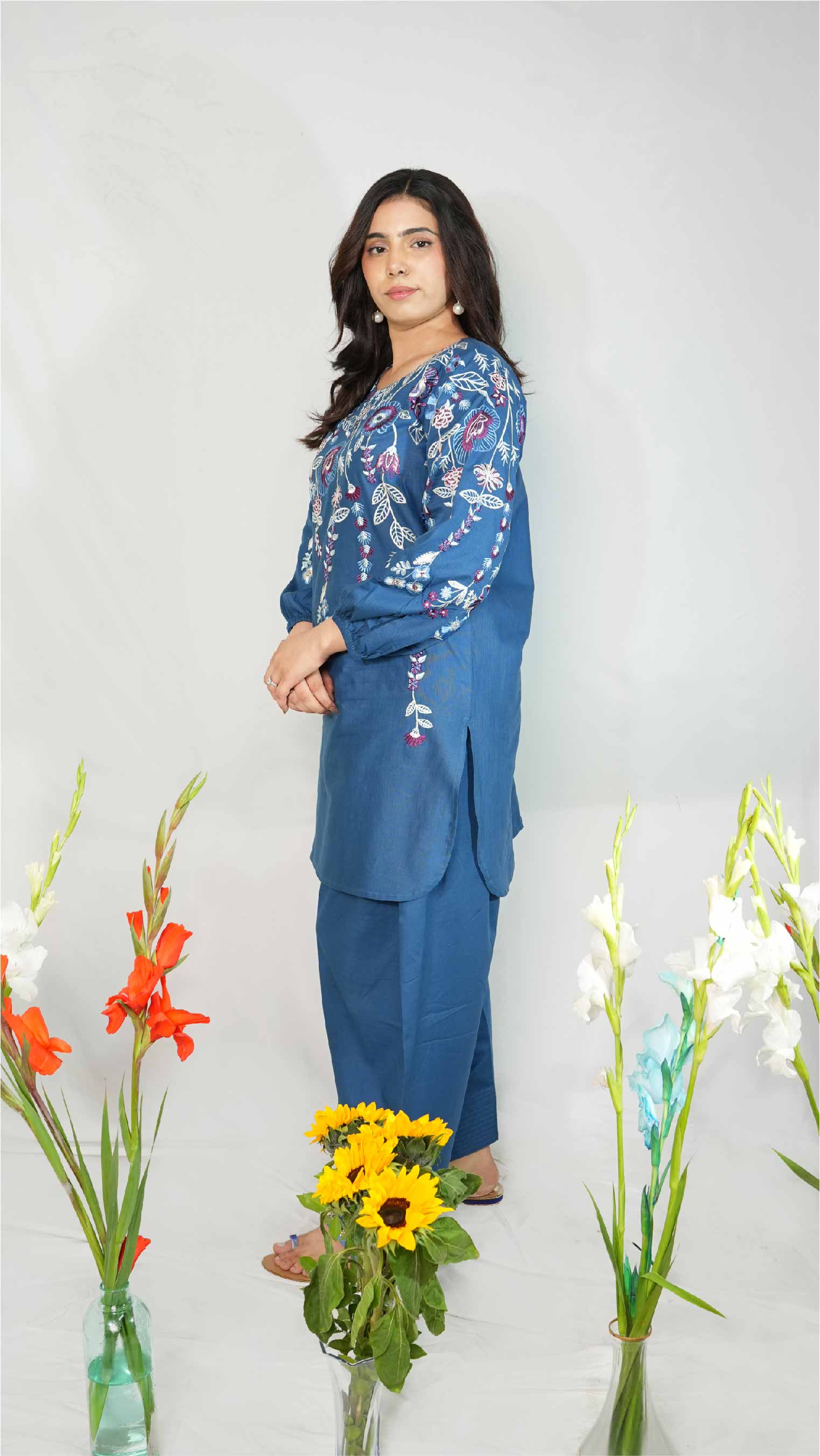 Woman in a blue floral outfit standing between flowers on a white background