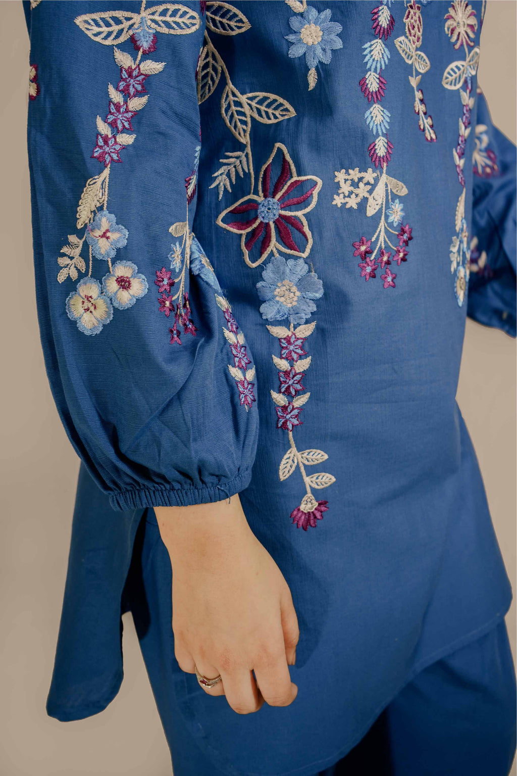 Blue embroidered garment with floral patterns on a neutral background