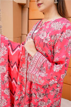 Person wearing a pink floral dress with intricate patterns, standing against a wooden panel background.