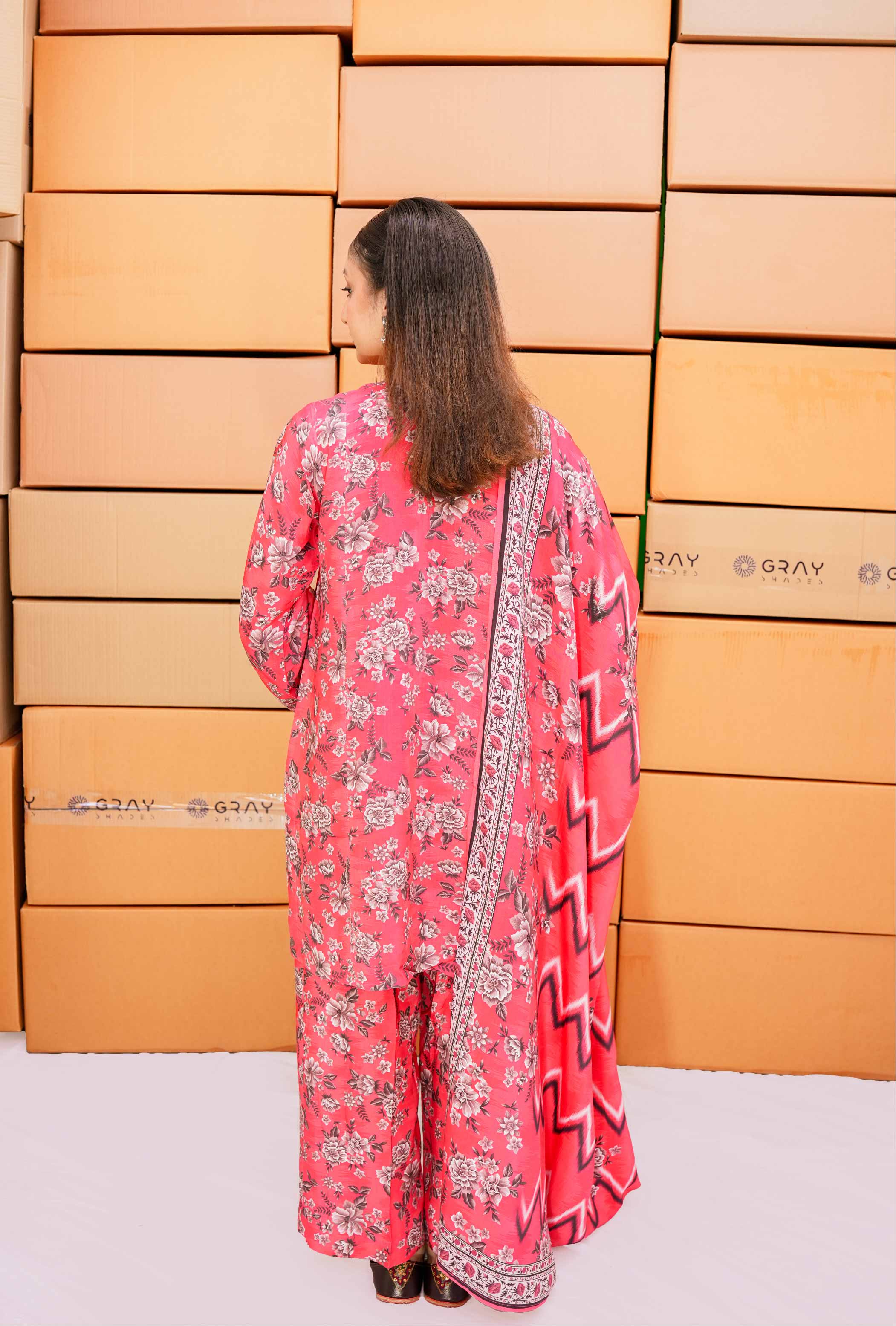Woman in a pink floral outfit standing in front of stacked boxes.