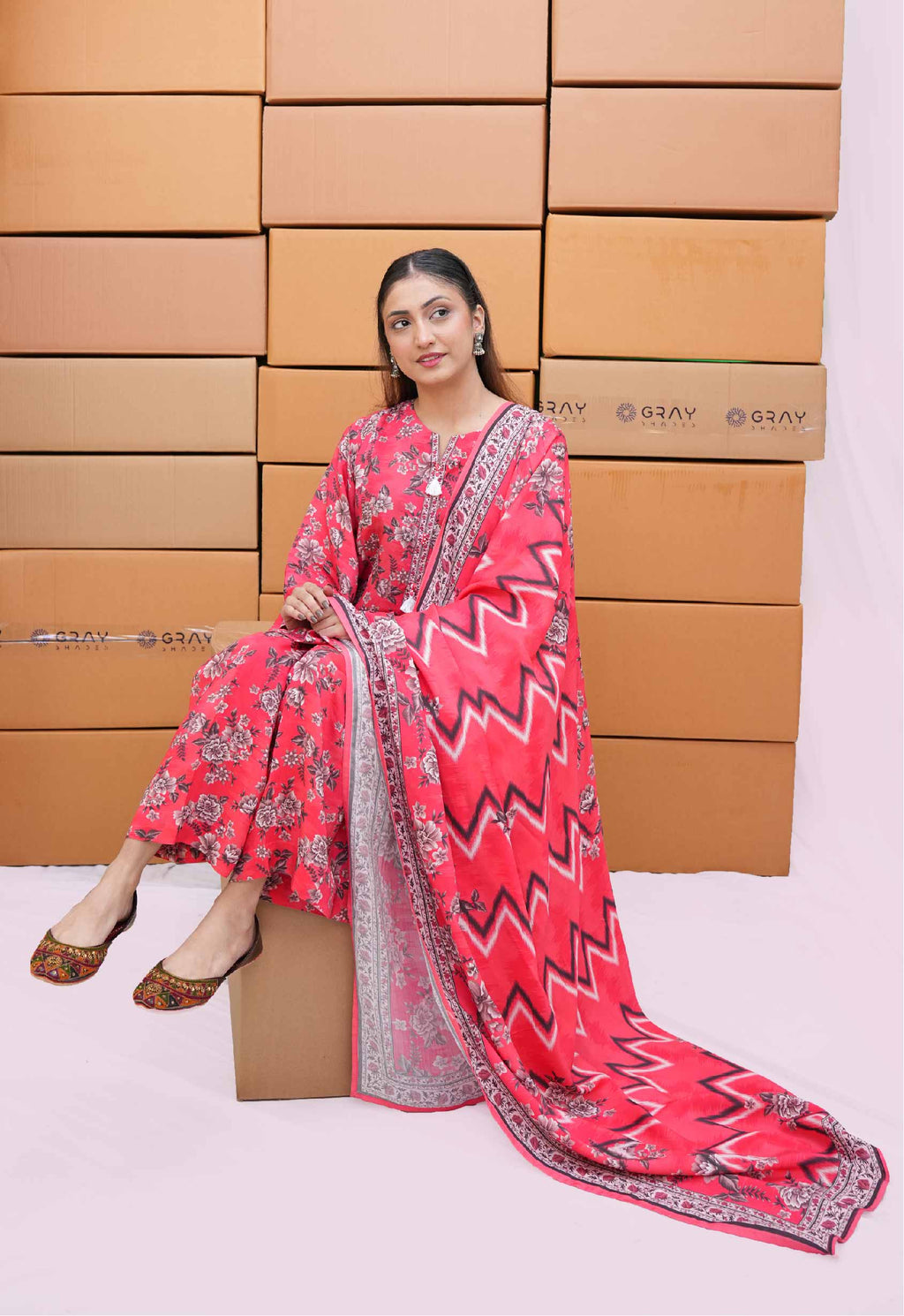 Woman in a red and pink traditional outfit sitting on a cardboard box with more boxes stacked behind her.
