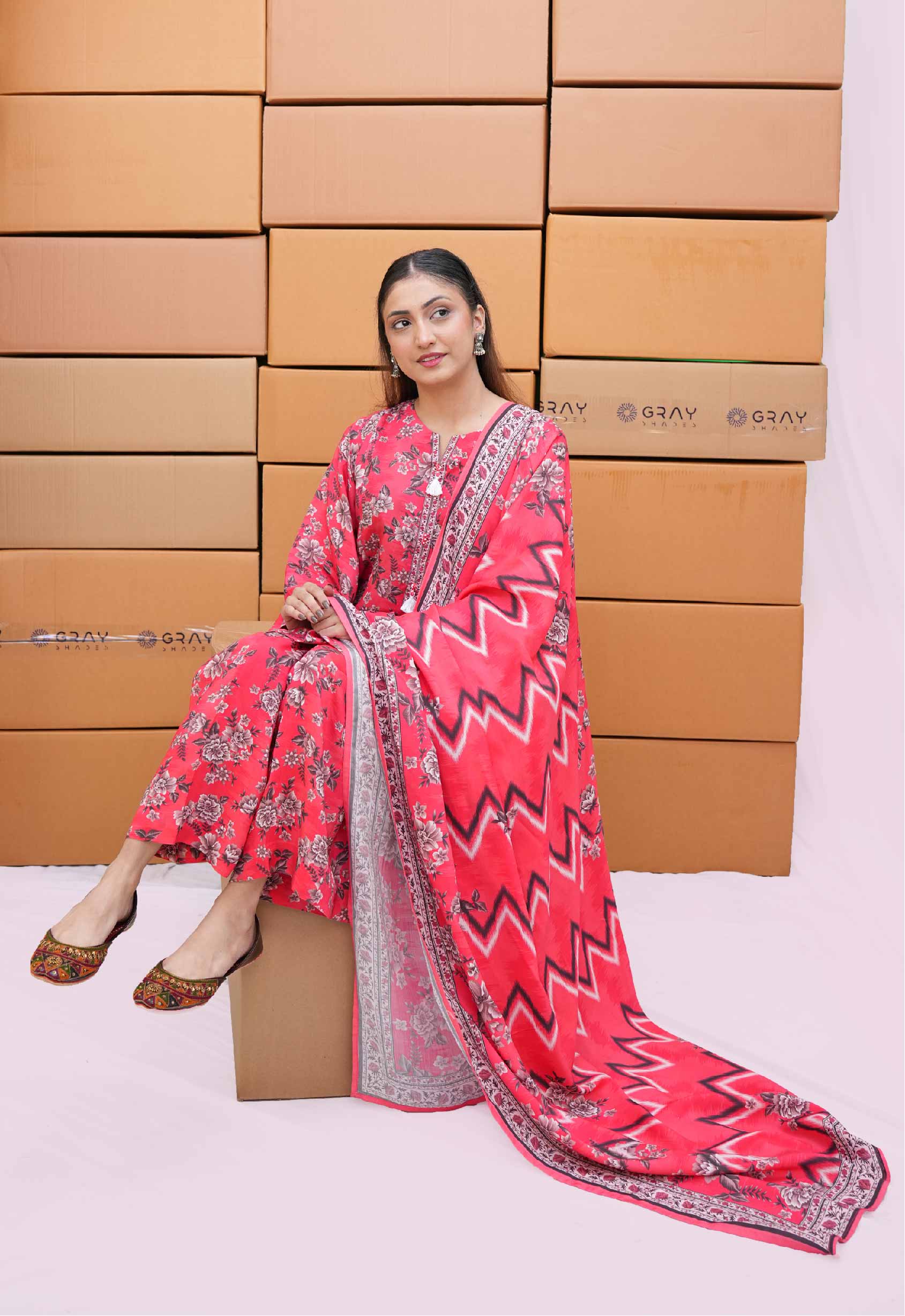 Woman in a red and pink traditional outfit sitting on a cardboard box with more boxes stacked behind her.