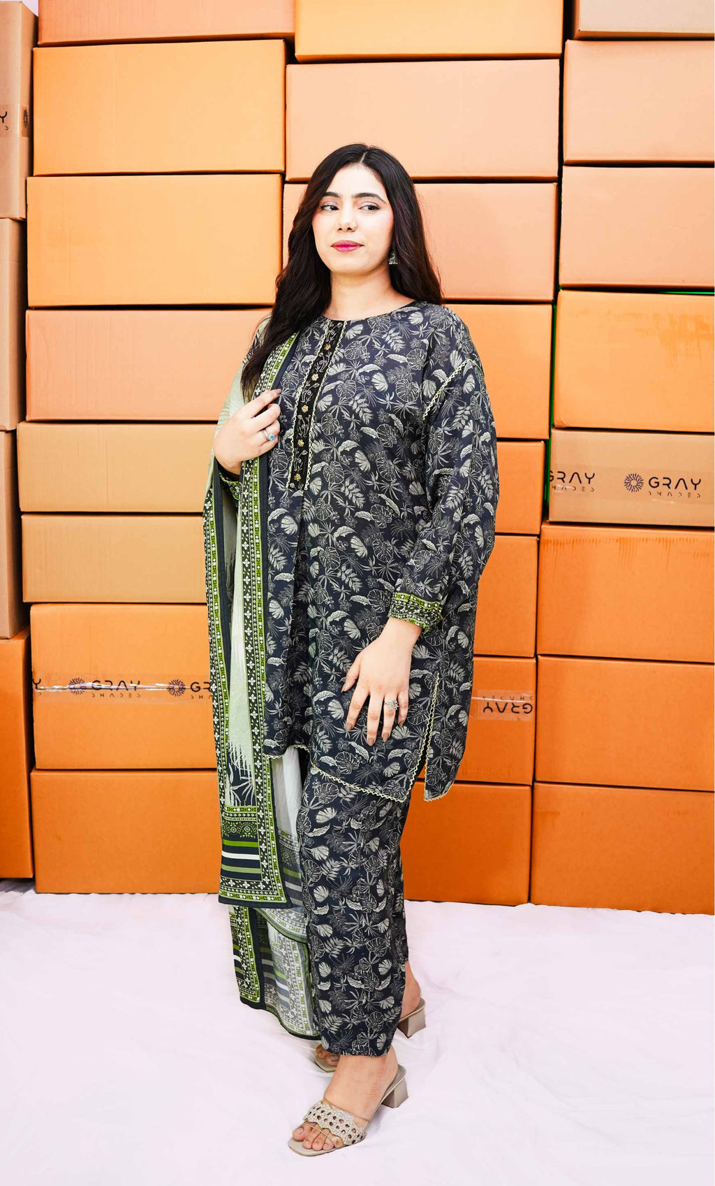Woman in a patterned outfit standing in front of orange boxes with 'Gray' branding.