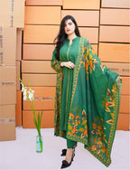 Woman in a green traditional outfit with floral patterns standing against orange cardboard boxes.