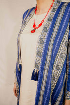 Blue patterned scarf with tassels and red necklace on a neutral background