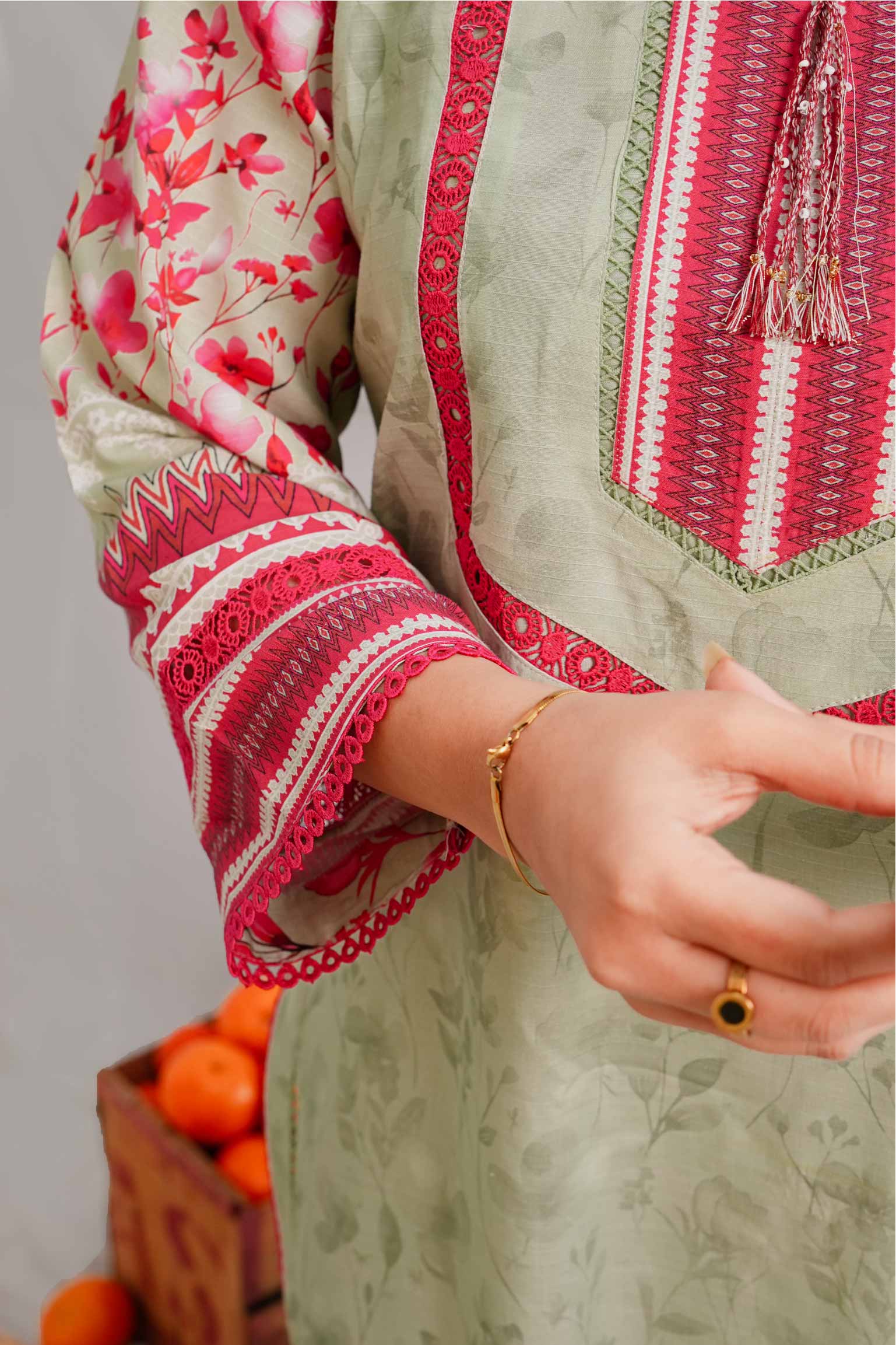 Close-up of a person wearing a traditional outfit with red and white embroidery, holding a basket of oranges.