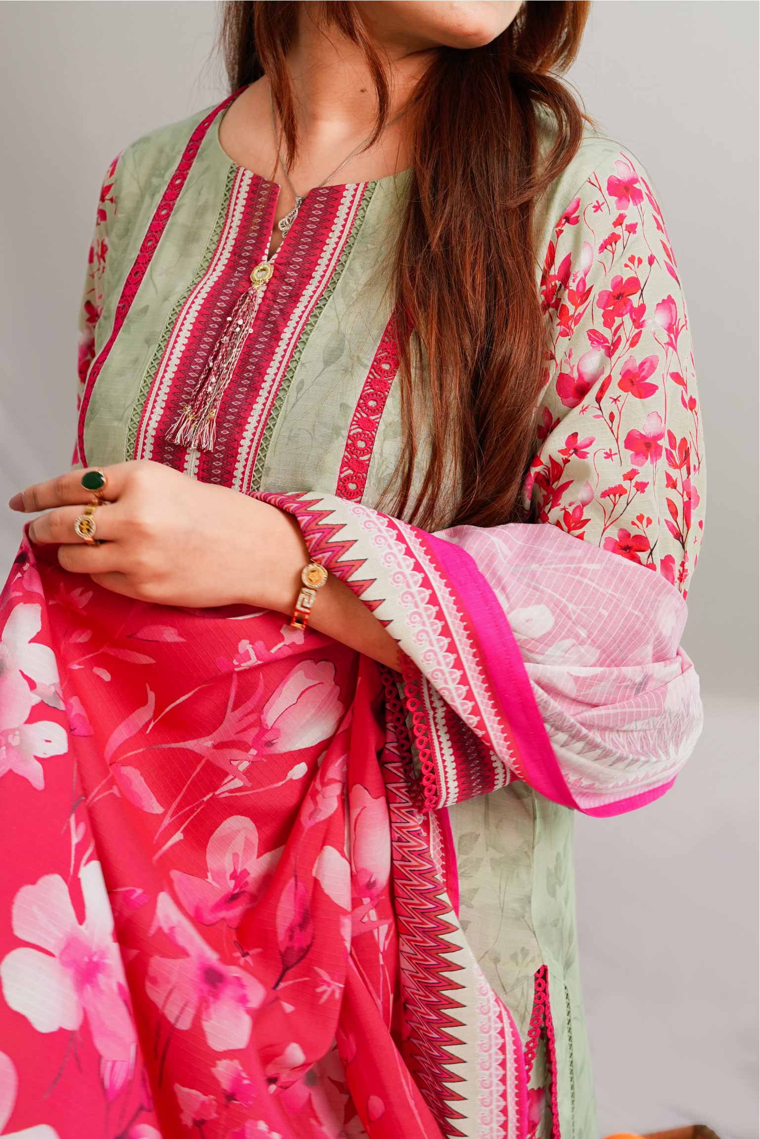 Woman wearing a floral pink and green traditional outfit with a white dupatta.
