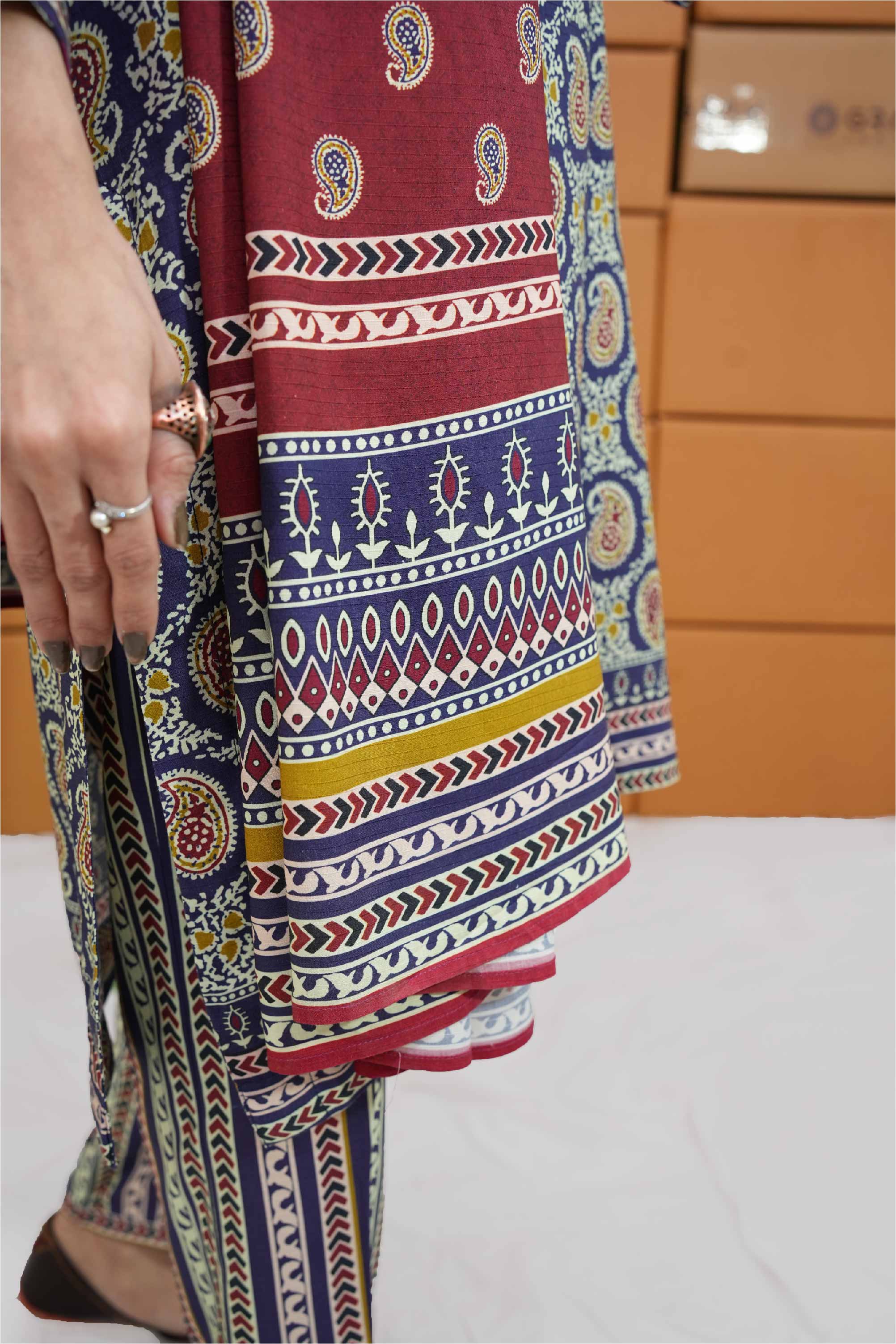 Colorful patterned fabric with a person's hand holding it, against a neutral background.