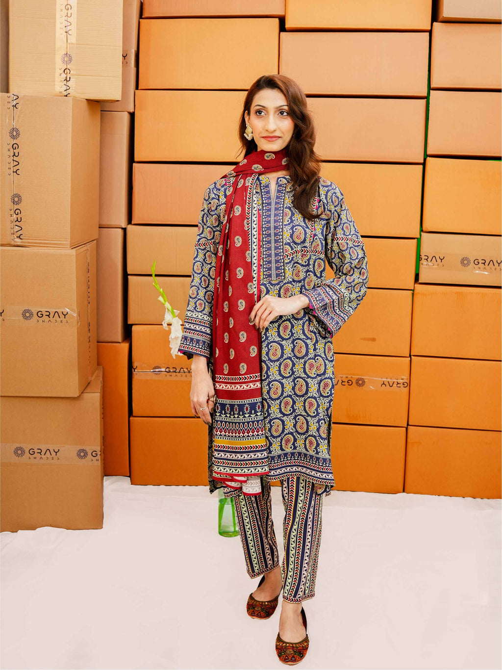 Woman in traditional outfit standing in front of stacked cardboard boxes