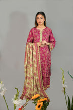 Woman wearing a pink and green traditional outfit with floral patterns, standing against a gray background with flowers in the foreground.