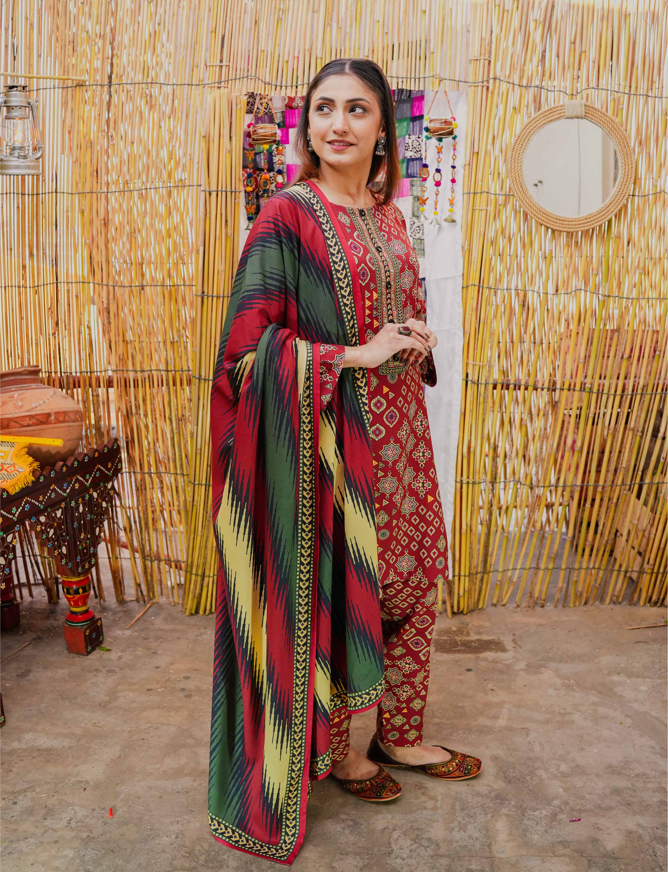 Woman in a colorful traditional outfit standing in front of a bamboo wall.