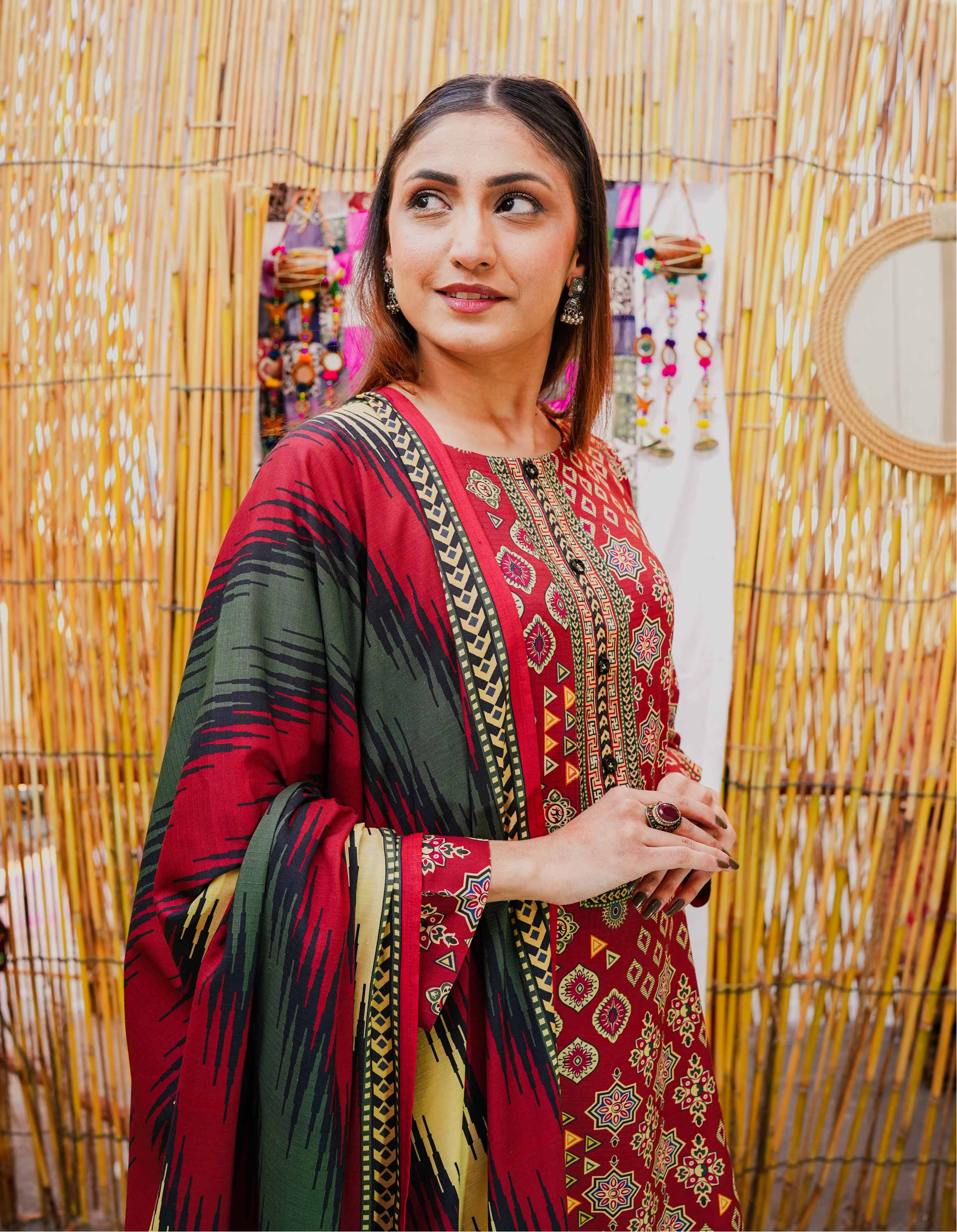 Woman in a red and green patterned dress standing in front of a decorative wall.