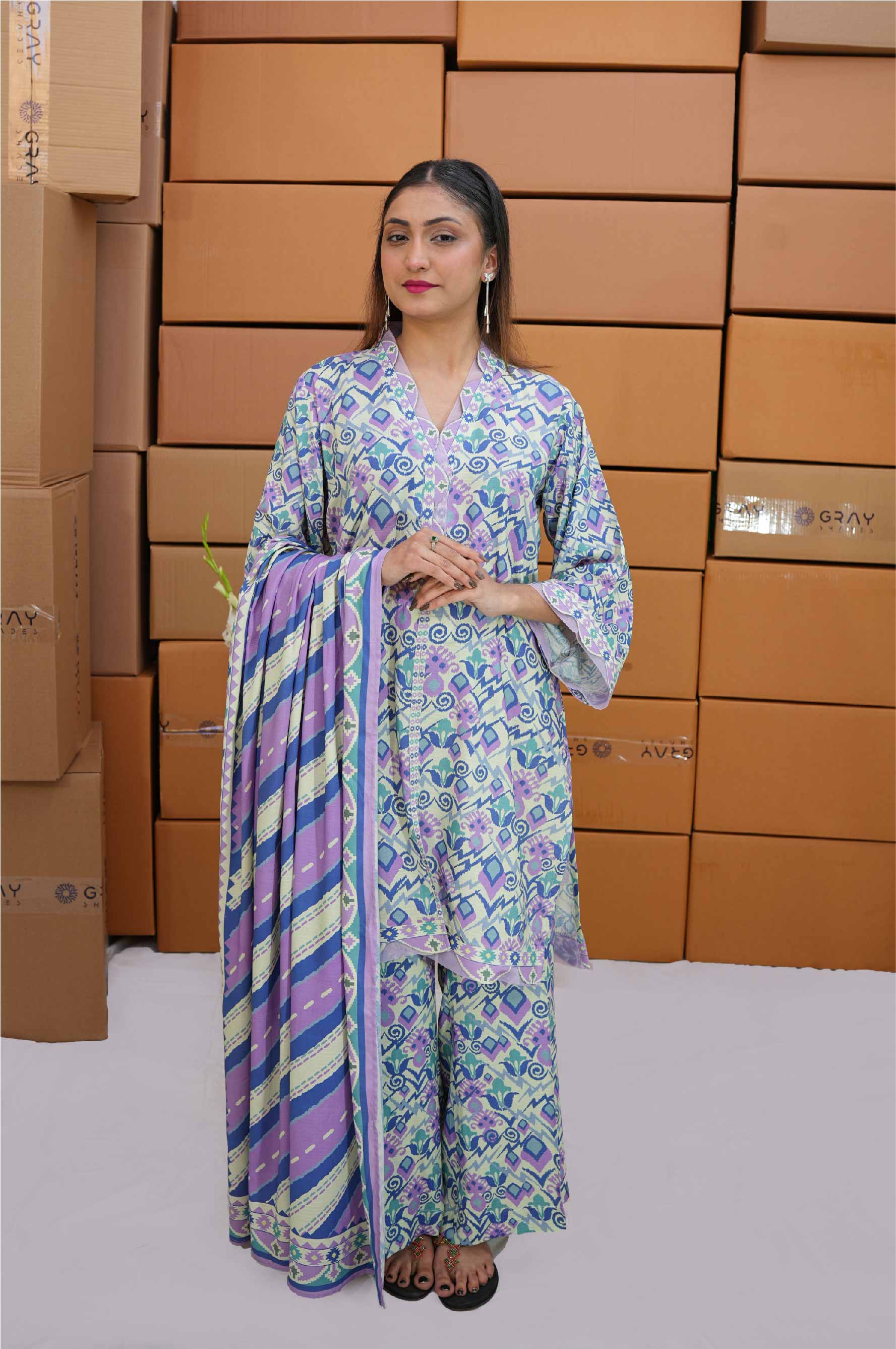 Woman in a floral outfit standing in front of stacked cardboard boxes