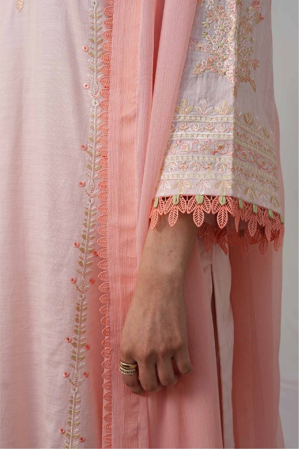 Close-up of a person wearing a light pink traditional outfit with intricate embroidery.