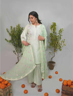 Woman in a light green traditional outfit standing among oranges and plants on a gray background
