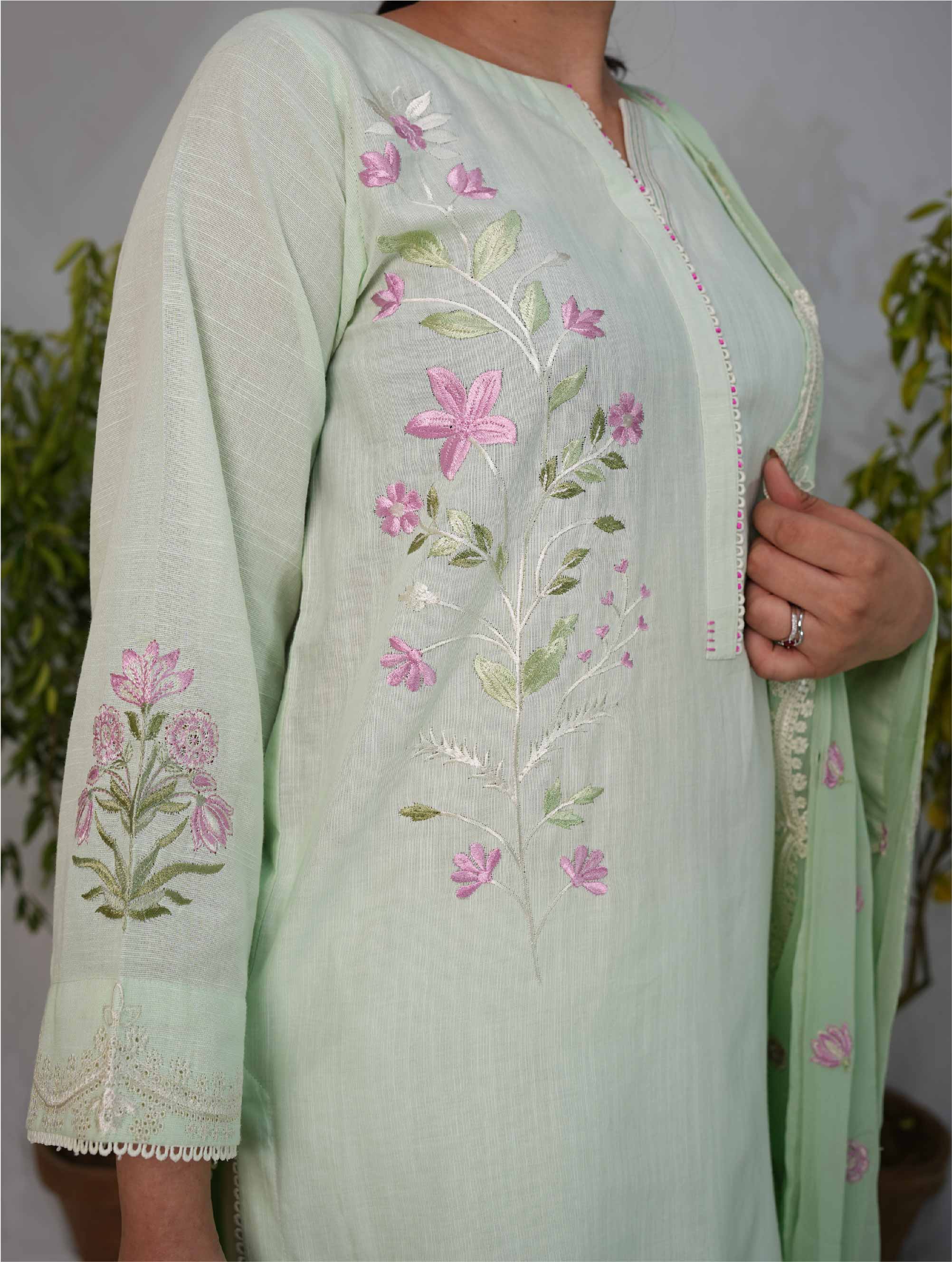 Light green embroidered outfit with floral patterns on a neutral background